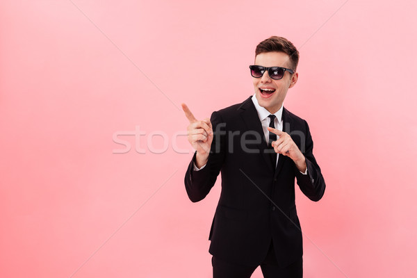 Young businessman i sunglasses pointing at copy space and smiling Stock photo © deandrobot