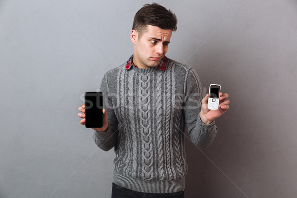 Picture of Displeased man in sweater choosing between smartphones Stock photo © deandrobot
