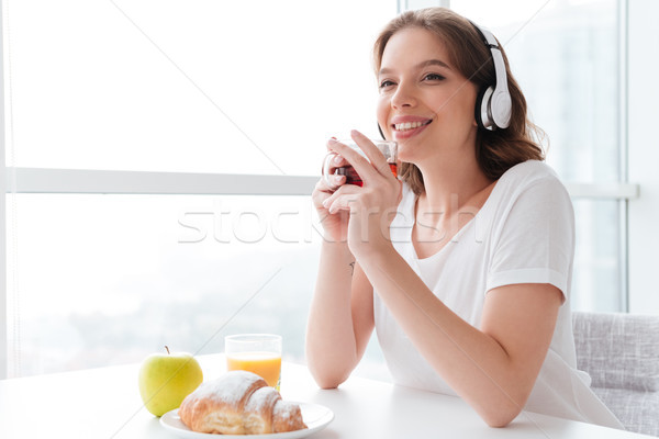 Cheerful young woman drinking tea listening music. Looking aside. Stock photo © deandrobot