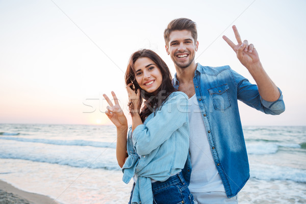 Couple standing and showing peace sign on the beach Stock photo © deandrobot