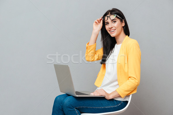 Young pretty woman sitting while using laptop over grey background Stock photo © deandrobot