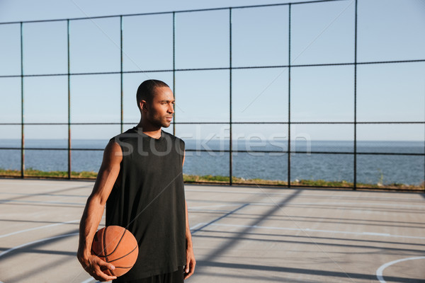 Serious afro american sportsman holding basketball and looking away Stock photo © deandrobot