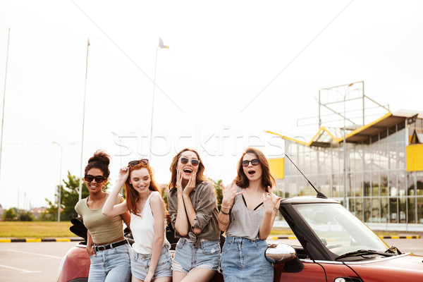 Happy four young women friends standing near car outdoors. Stock photo © deandrobot