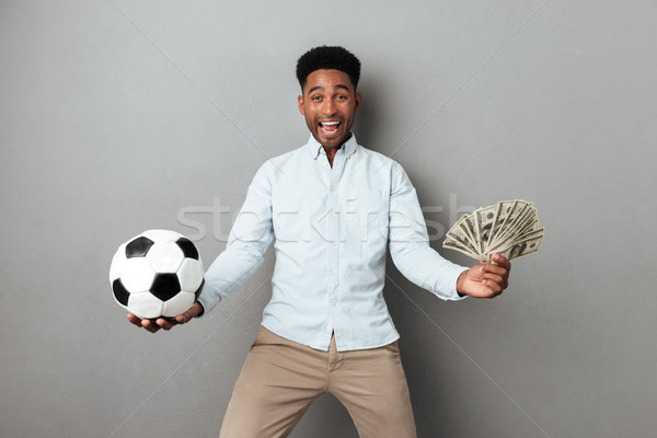 Happy smiling african man holding football and money banknotes Stock photo © deandrobot