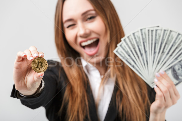 Smiling winking woman showing bitcoin and olding dollars in hands isolated Stock photo © deandrobot