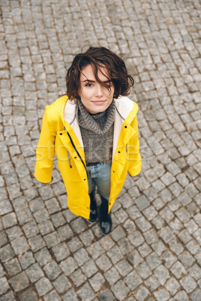 Portrait of cute female in yellow stylish coat looking up on cam Stock photo © deandrobot