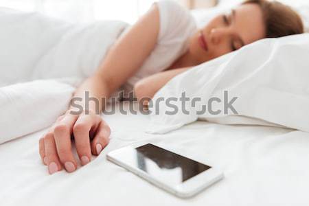 Sleeping young woman lies in bed near phone. Stock photo © deandrobot