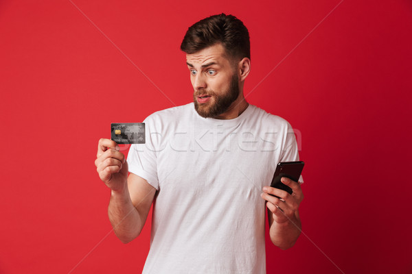 Nervous young man holding mobile phone and credit card. Stock photo © deandrobot