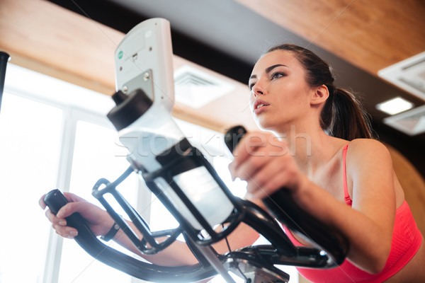 Focused sportswoman exercising on bicycle in gym Stock photo © deandrobot