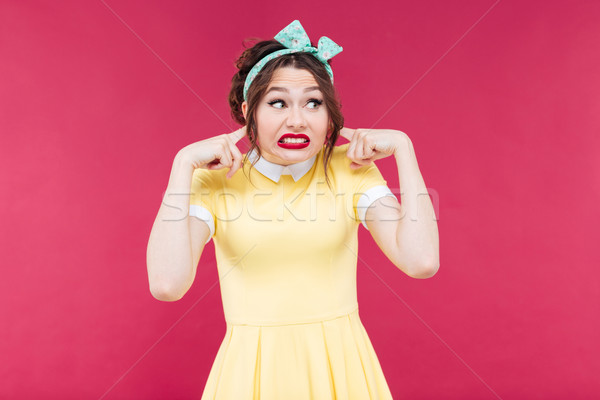 Stock photo: Cute irritated pinup girl closed her ears by fingers