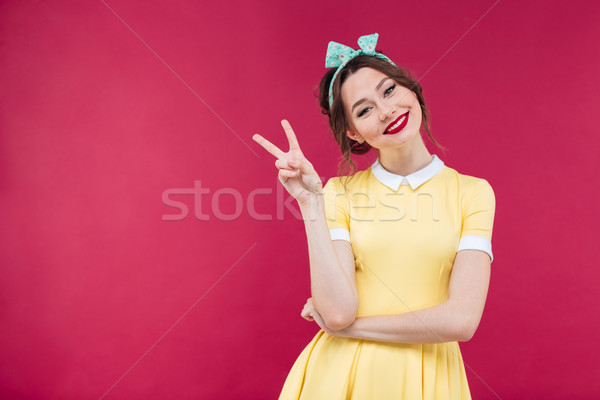 Smiling charming young woman in yellow dress showing peace sign Stock photo © deandrobot