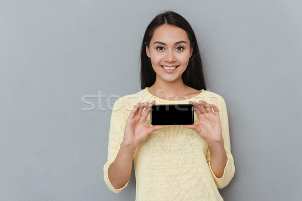 Cheerful attractive young woman holding blank screen cell phone Stock photo © deandrobot