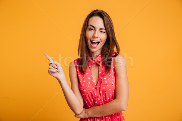 Happy brunette woman in dress winks and pointing up Stock photo © deandrobot