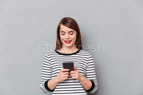 Portré mosolygó nő sms chat mobiltelefon izolált szürke Stock fotó © deandrobot