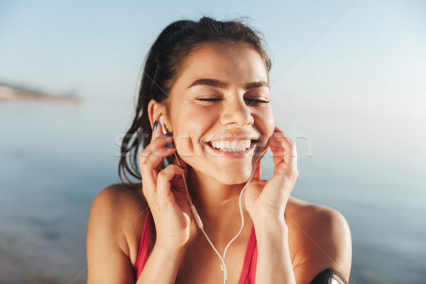 Cheerful sports woman listening music in earphones with closed eyes Stock photo © deandrobot