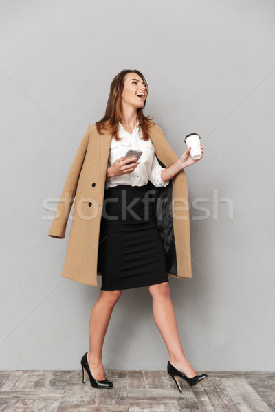 Happy young business woman holding coffee chatting by phone. Stock photo © deandrobot