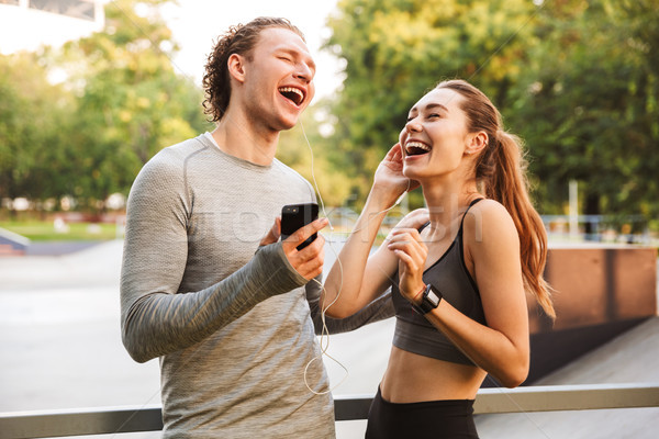 Sport loving couple friends in park outdoors listening music with earphones. Stock photo © deandrobot