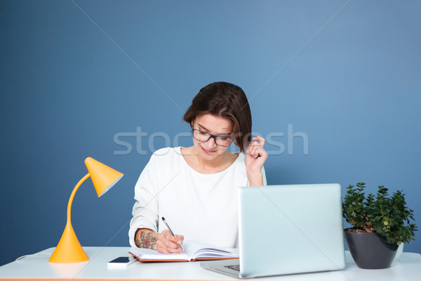 Smiling young woman sitting and writing in notebook Stock photo © deandrobot