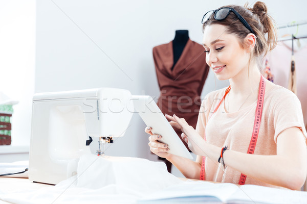 Smiling woman seamstress sitting and using tablet at work Stock photo © deandrobot