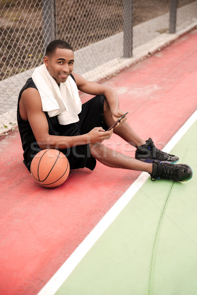 African basketball player sitting in the park and holding tablet Stock photo © deandrobot