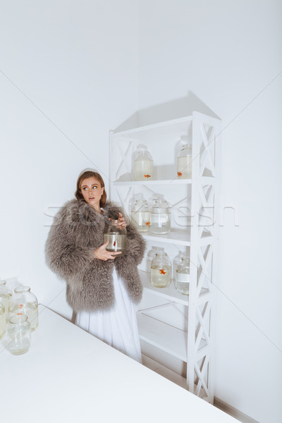 Attractive woman wearing fur coat holding gold fish in jar Stock photo © deandrobot