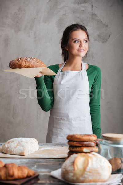 Young happy lady baker standing and holding bread. Stock photo © deandrobot