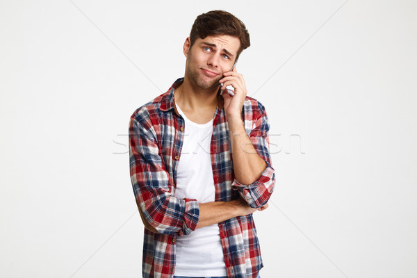 Portrait of a doubtful young man talking on mobile phone Stock photo © deandrobot