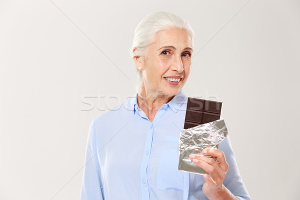 Portrait of charming old lady holding chocolate bar, looking at  Stock photo © deandrobot
