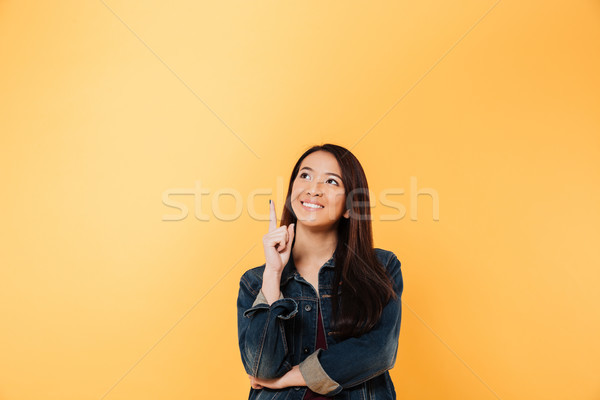 Smiling asian woman in denim jacket pointing and looking up Stock photo © deandrobot