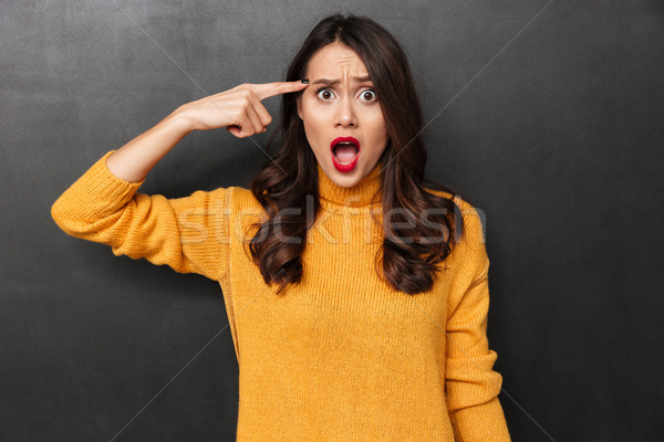 Confused brunette woman in sweater holding finger on temple Stock photo © deandrobot