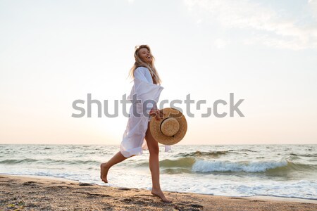 Beautiful young blonde woman with hat walking at the beach. Stock photo © deandrobot