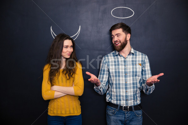 Smiling couple imitating devil and angel over chalkboard background Stock photo © deandrobot