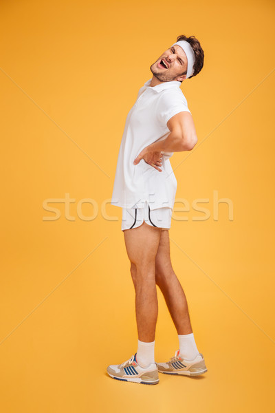 Stressed young fitness man standing and suffering from back ache Stock photo © deandrobot