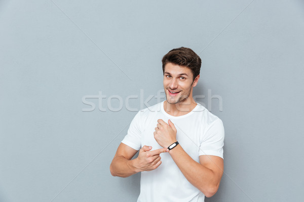 Stock photo: Cheerful young man standing and pointing on fitness tracker