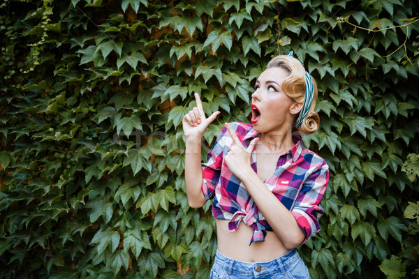 Amazed pin up girl with opened mouth pointing away Stock photo © deandrobot
