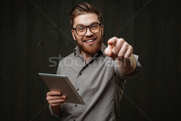 Man in eyeglasses holding tablet computer and pointing at camera Stock photo © deandrobot