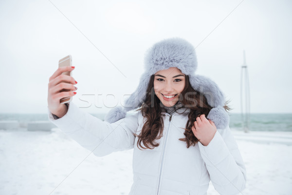 Cheerful woman wearing hat make selfie by her phone. Stock photo © deandrobot