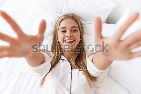 Happy young lady dressed in pajama lies in bed Stock photo © deandrobot