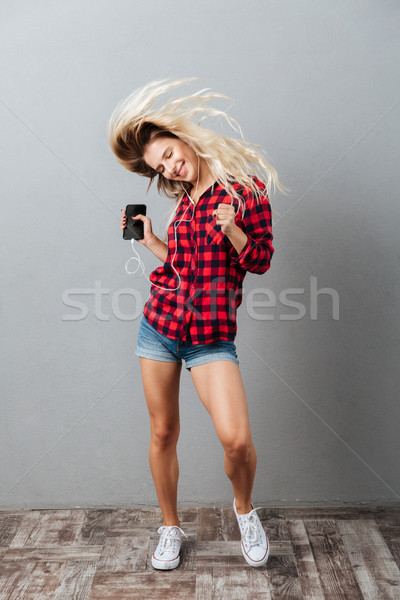 Happy young blonde woman listening music by phone shaking hair. Stock photo © deandrobot