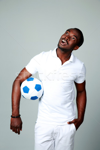 Surprised african man with soccer ball looking up on gray background Stock photo © deandrobot