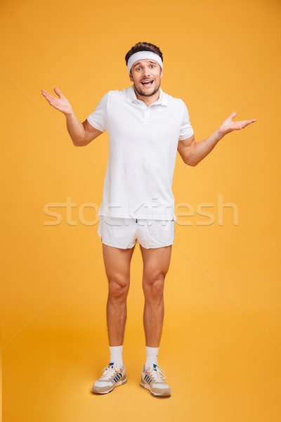 Confused young sportsman standing and holding copyspace on palms Stock photo © deandrobot