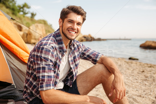 Smiling man tourist sitting in touristic tent at the beach Stock photo © deandrobot