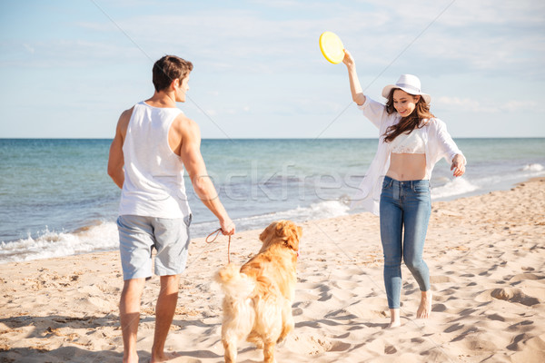 Young beautiful couple playing with their dog on the beach Stock photo © deandrobot