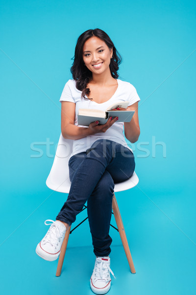 Smiling young vietnamese girl reading book and sitting on chair Stock photo © deandrobot