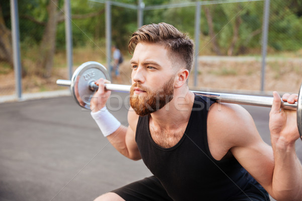 Concentrated bearded sports man doing squatting exercises with barbell Stock photo © deandrobot