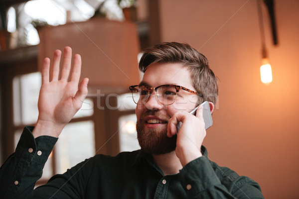 Cheerful man talking by phone and waving look aside. Stock photo © deandrobot