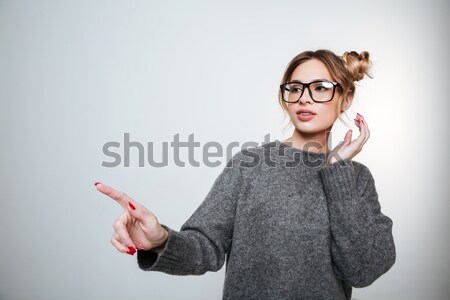 Charming smiling young woman in glasses standing and pointing away Stock photo © deandrobot