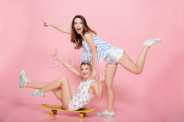 Dos alegre mujeres skateboard senalando lejos Foto stock © deandrobot