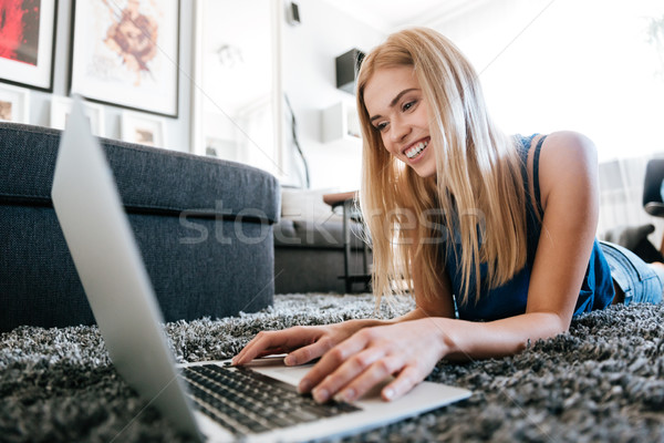 Cheerful woman lying on carpet and using laptop at home Stock photo © deandrobot
