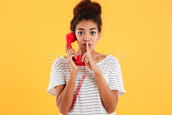 Beautiful lady showing silence gesture while talking on red handset Stock photo © deandrobot